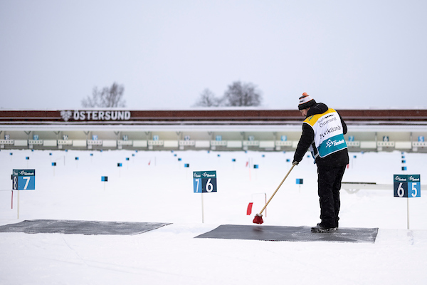 Man står med ryggen mot kameran och sopar en skjutmatta. Det står funktionär på ryggen